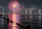 小雨の夜の東京湾に上がる打ち上げ花火と湾岸の夜景