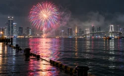 小雨の夜の東京湾に上がる打ち上げ花火と湾岸の夜景