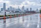 雨上がりの港沿いの道路に並ぶコーンと柵、奥に高層ビルと観覧車が見える市民マラソンのコース