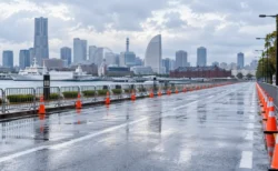 雨上がりの港沿いの道路に並ぶコーンと柵、奥に高層ビルと観覧車が見える市民マラソンのコース