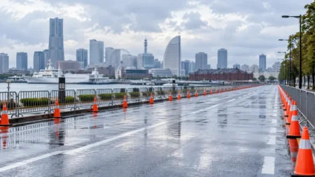 雨上がりの港沿いの道路に並ぶコーンと柵、奥に高層ビルと観覧車が見える市民マラソンのコース