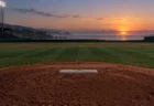 夜明けの空と海を背に、ナイター照明が灯る無人の野球場のマウンド