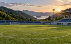 緑の山々と海を望む小さなサッカースタジアムの芝生、センターサークルに置かれたボール