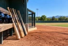 晴れた大学野球グラウンドのベンチ前に並ぶ木製バットとヘルメット