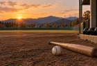 秋の夕方の地方球場の内野グラウンドに置かれた硬式球とバット
