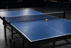 照明に照らされた無人の競技フロアの青い卓球台とオレンジのボール