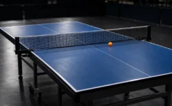 照明に照らされた無人の競技フロアの青い卓球台とオレンジのボール