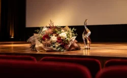 映画館のスクリーン前の舞台に置かれた花束とトロフィー