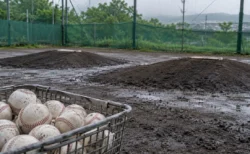 雨上がりの高校野球のブルペンに置かれた、白い硬式ボールが入ったかご