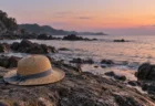 夏の夕方の日本海の磯に打ち寄せる穏やかな波と、岩の上に置かれた子ども用の麦わら帽子