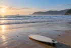 朝の遠浅の砂浜に寄せる白い波と砂の上に置かれたサーフボード