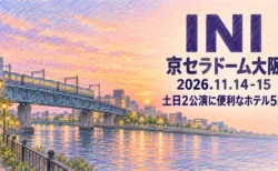 INI 京セラドーム大阪 2026.11.14-15 土日2公演に便利なホテル5選の文字と、夕暮れの川と鉄橋を走る電車を描いた色鉛筆画
