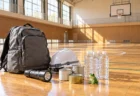 中学校の体育館の床に並べられた非常用持ち出し袋と、カエルの小さな置物