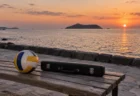 海辺の夕暮れのベンチに置かれたバレーボールとフルートケース
