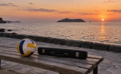 海辺の夕暮れのベンチに置かれたバレーボールとフルートケース