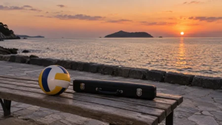 海辺の夕暮れのベンチに置かれたバレーボールとフルートケース
