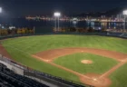 夜の野球場のスコアボード横の照明塔と、延長戦の続くグラウンド
