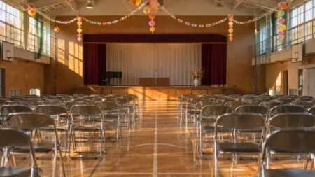 秋の午後の中学校の体育館、ステージ前に並ぶパイプ椅子とマイクスタンド