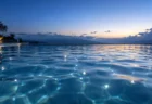 夜明け前の屋外プールの水面に、青い光の反射と波紋が広がるイメージ