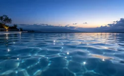 夜明け前の屋外プールの水面に、青い光の反射と波紋が広がるイメージ