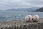 曇り空の日本海を背に、コンクリートの堤防に並んで置かれた2つの硬式球