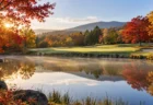 秋の朝のゴルフコースの池越しのグリーンと紅葉