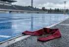 雨に濡れた陸上競技場のトラックとロードの境目に置かれた、えんじ色の駅伝のたすき