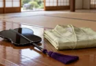 木の床に置かれた、房の付いた漆塗りの軍配と、たたまれた淡い緑の絹の着物