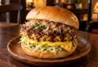 喫茶店の木のテーブルに置かれた、お好み焼とキャベツ、オムレツを挟んだバーガー