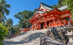 晴れた青空の下、朱塗りの神社社殿と石段