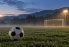 夜明け前の練習グラウンドの芝に置かれたサッカーボールと照明に照らされたゴール