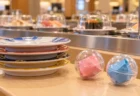 回転寿司のカウンターに置かれた寿司皿と、小さなカプセルトイの景品が入った透明カプセル