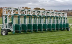 曇り空の下、芝コースに置かれた競馬のスターティングゲート