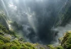 霧に包まれた巨大な縦穴を断崖の縁から見下ろす風景