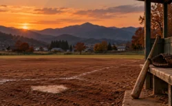 秋の夕暮れ、山並みを望む町の野球場。土のグラウンドのホームベースと、ベンチに立てかけた木製バットと革のグローブ
