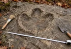 灰色の砂岩の地層面に残る大きな恐竜の足跡のくぼみと、そばに置かれた発掘用の刷毛と巻き尺