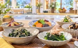 明るいキッチンスタジオの調理台に並ぶ、野菜の和え物や煮物の小鉢料理のイメージ