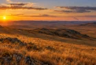 夕暮れの斜光に照らされた秋の乾いた草原と、地平線の遠くに立ちのぼる煙