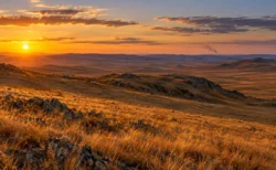 夕暮れの斜光に照らされた秋の乾いた草原と、地平線の遠くに立ちのぼる煙