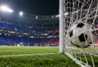 ナイター照明に照らされたスタジアムでゴールネットに収まったサッカーボール