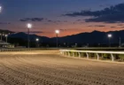 夕暮れに照明がともる地方競馬場の無人のダートコース