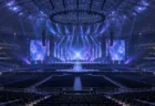 開演前のドーム会場で、青と紫のライトが無人のステージを照らす様子