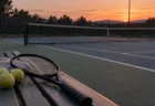 夕暮れの屋外テニスコートとベンチに置かれたラケット