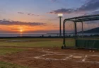 夕暮れの野球場で打撃練習用ケージとホームベース