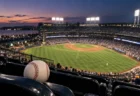 夕暮れのナイター照明が灯る大きな野球場と、客席に置かれた硬式球のイメージ