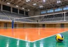照明に照らされた体育館のバレーボールコートとネット、床に置かれたボール