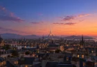 夕暮れの空の下に尖塔の光る城が見える丘の上の街並み