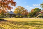 秋の住宅街にある公園の芝生広場と遊具、奥に低い建物が並ぶ穏やかな昼の風景