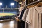 ハンガーに並ぶユニフォーム風シャツと背景の夜の野球場スタンド