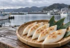 漁港を背景に、竹ざるに並んだ焼き目のついた笹かまぼこと笹の葉